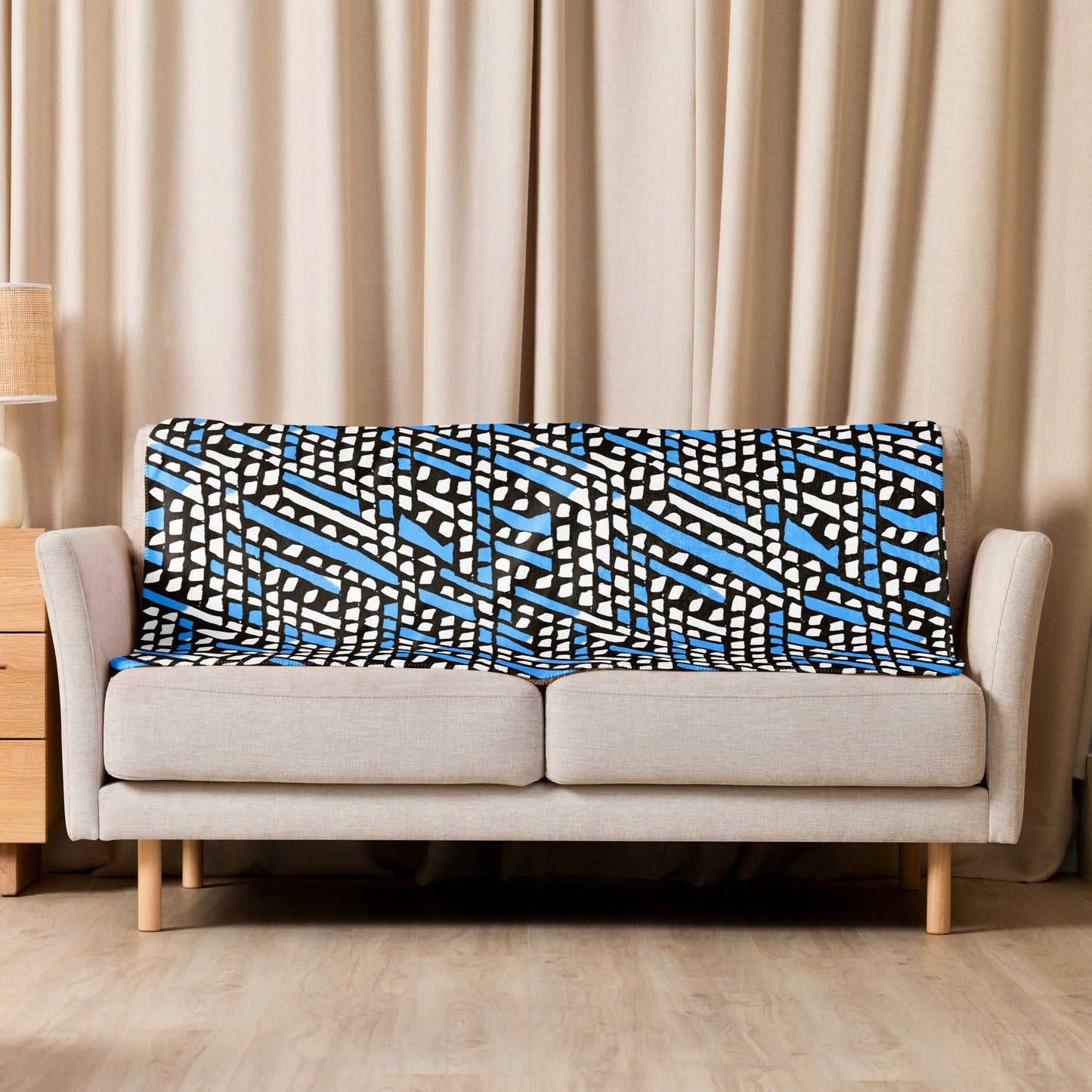 The blue Ilorin Sherpa blanket from Tintin Studios laid on a cream couch, providing a touch of rustic elegance with its subtle patterns and soft texture.