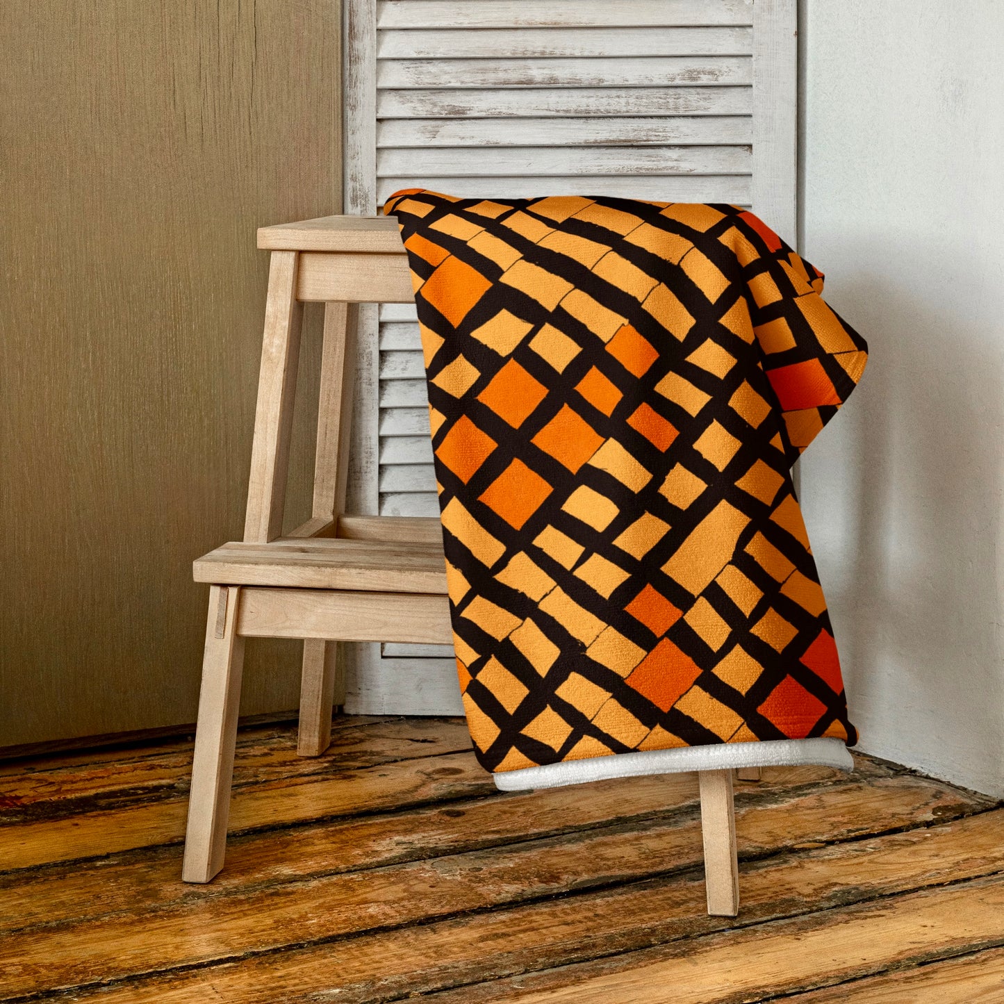 Orange Lagos beach towel from Tintin Studios folded elegantly on a wooden stool, highlighting its chic and contemporary style.