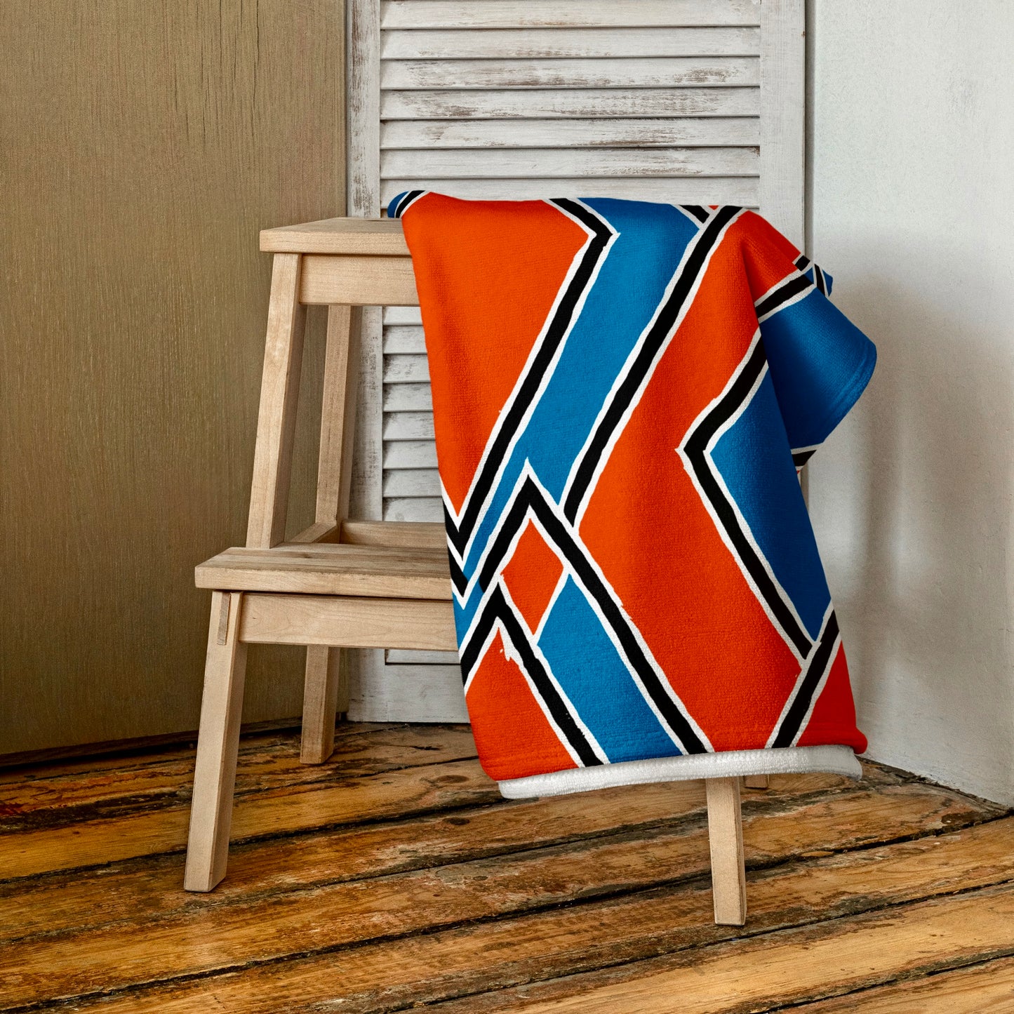Bright red Nana towel from Tintin Studios elegantly folded and draped over a rustic wooden stool, showcasing its intricate patterns and vibrant hue that pops against the natural wood.