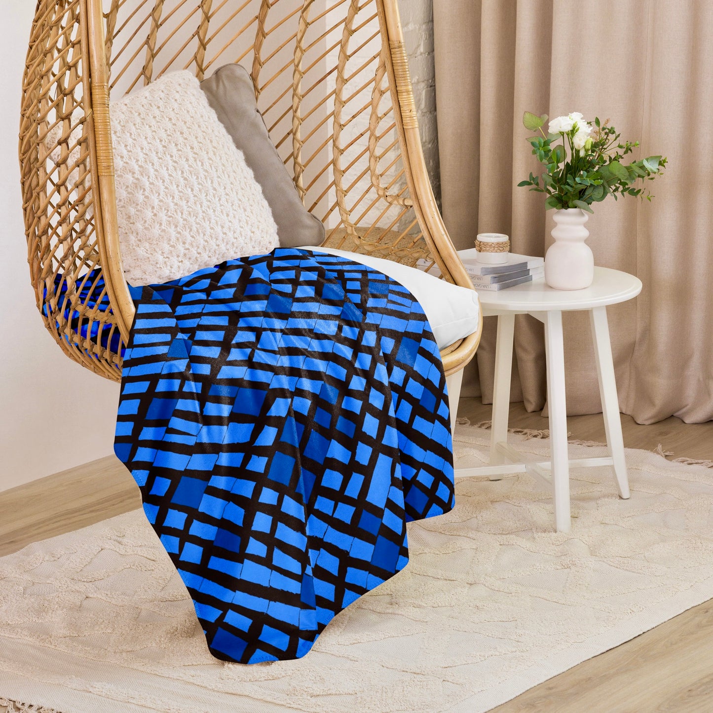 Chic blue Lagos Sherpa blanket in a captivating abstract design draped over a hanging wicker chair, infusing a creative and cosy element into a modern home setting.