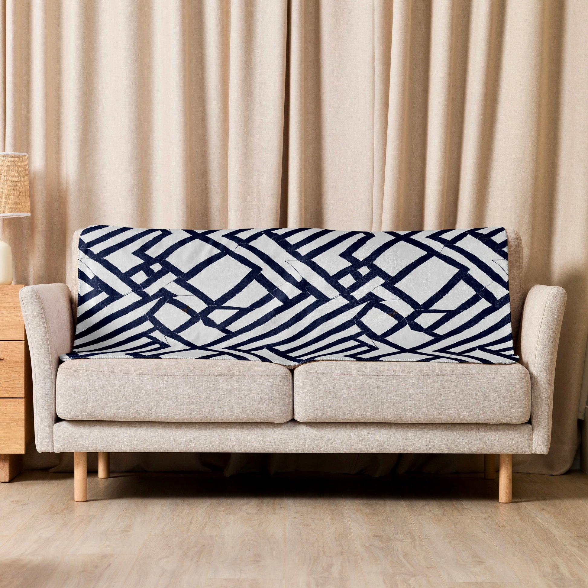 Tintin Studios' blue geometrically patterned Lokoja Sherpa blanket elegantly draped over a cream couch, complementing the modern aesthetic of the living space.