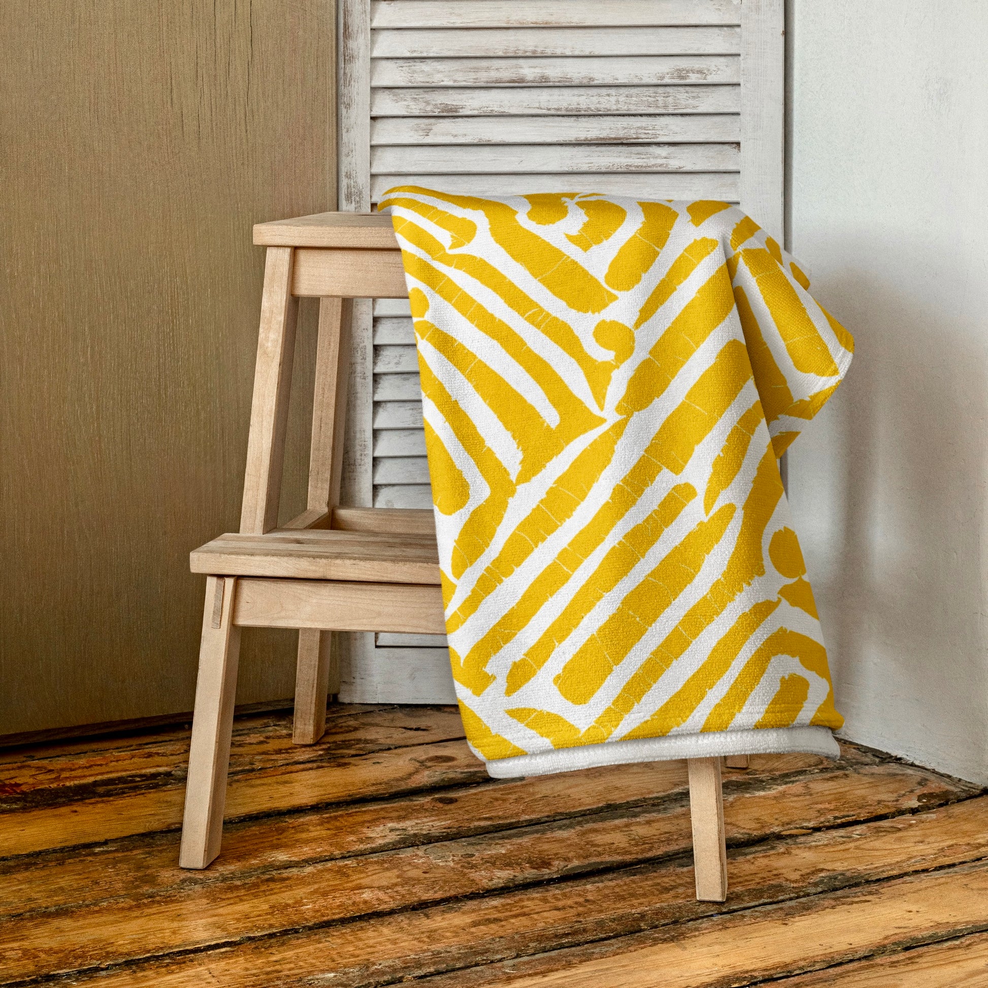 Vibrant yellow ChiChi beach towel from Tintin Studios, neatly folded on a wooden stool, displaying its understated elegance and modern design.