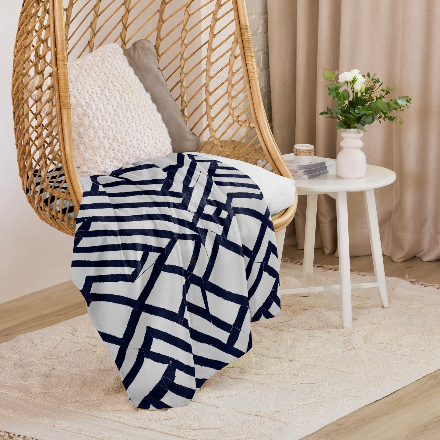 Lokoja Sherpa blanket from Tintin Studios featuring geometric blue patterns draped on a wicker chair, enhancing the ambience with its contemporary style and snug feel.