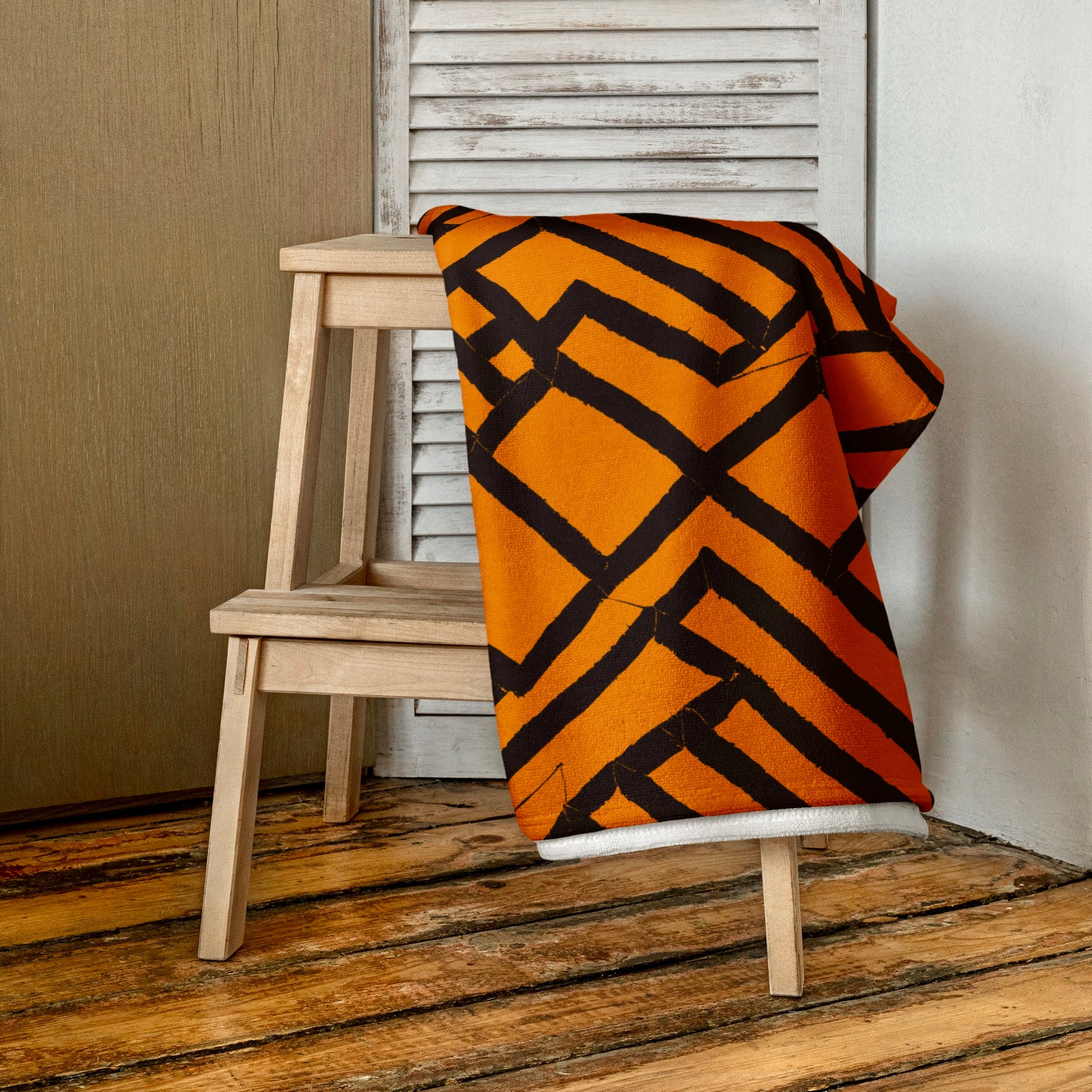 Orange Lokoja beach towel from Tintin Studios, elegantly folded and draped over a wooden stool, highlighting the richness of its color and intricate pattern details.