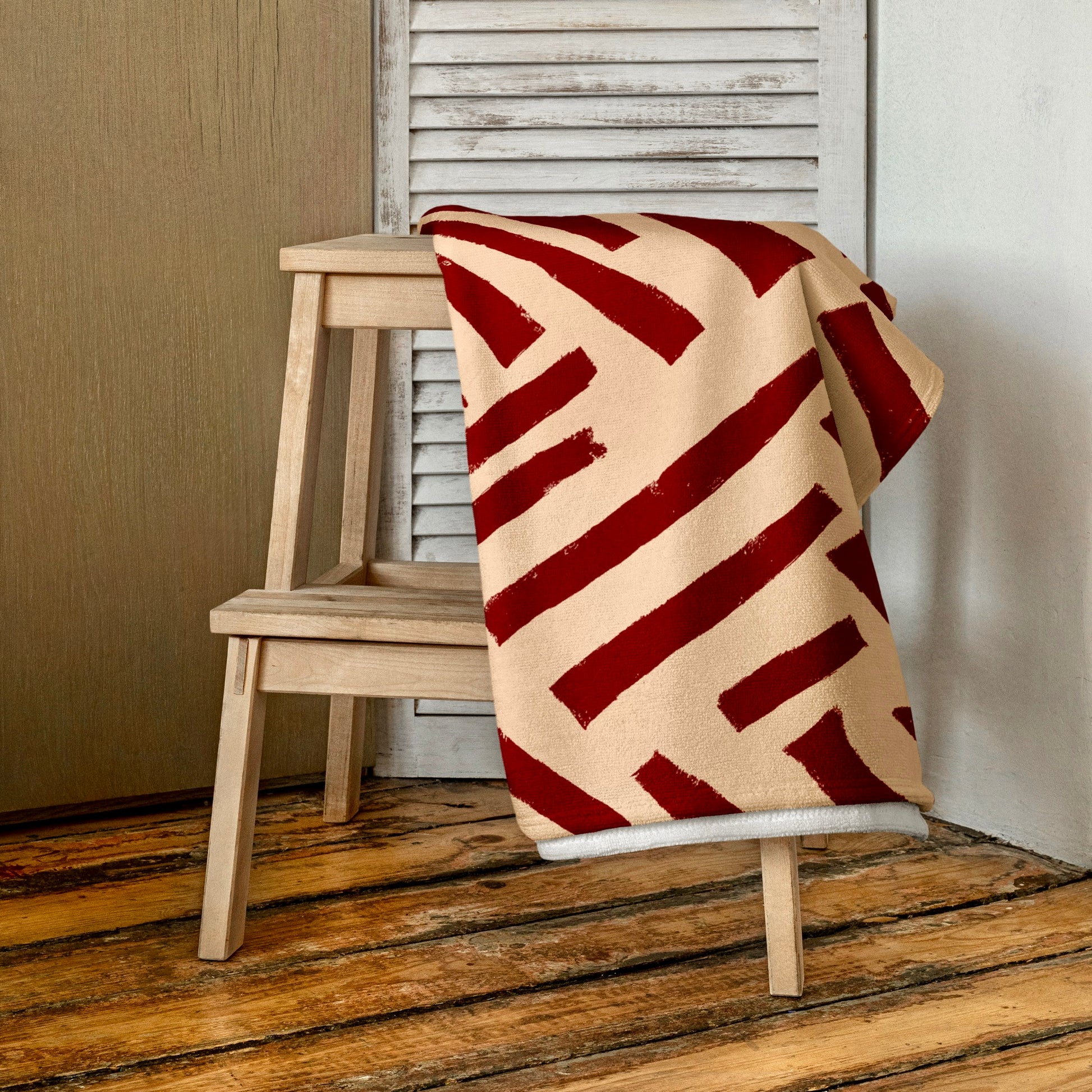 Red Tutu beach towel from Tintin Studios folded and draped elegantly over a wooden stool, showcasing its vivid red hue and lively abstract motifs that capture attention.