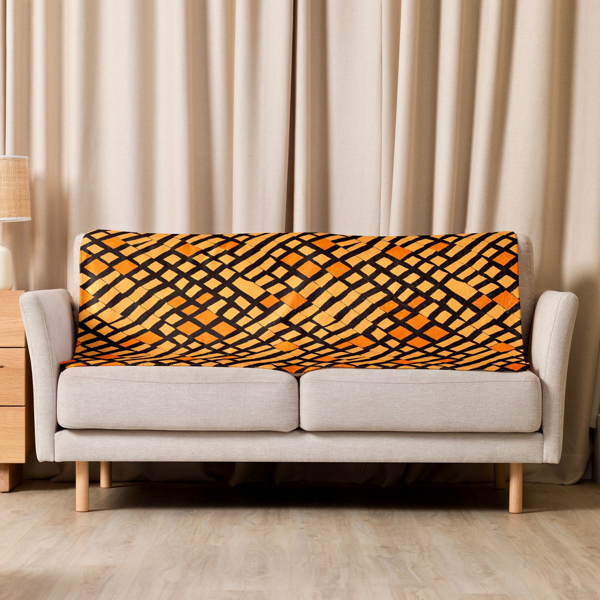 Orange Lagos Sherpa blanket from Tintin Studios with vibrant abstract designs thrown casually over a cream couch, providing a pop of colour and artistic flair to the living area.