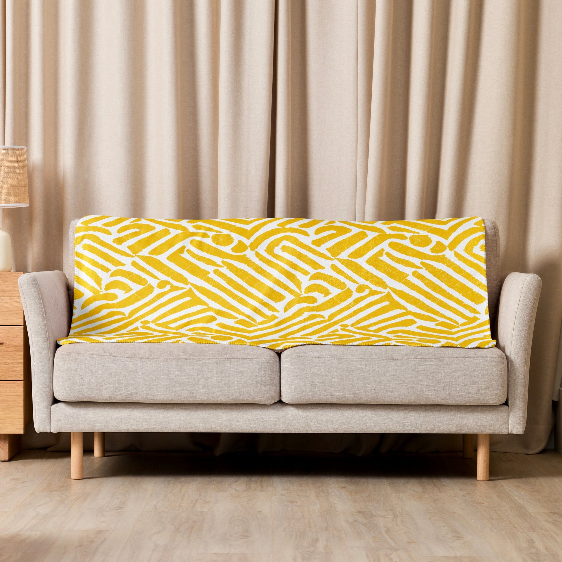 ChiChi Sherpa blanket from Tintin Studios casually draped over a cream couch in a well-lit living room, illustrating the blanket’s vibrant yellow and white design that perfectly complements modern home décor and offers a cosy, inviting look.