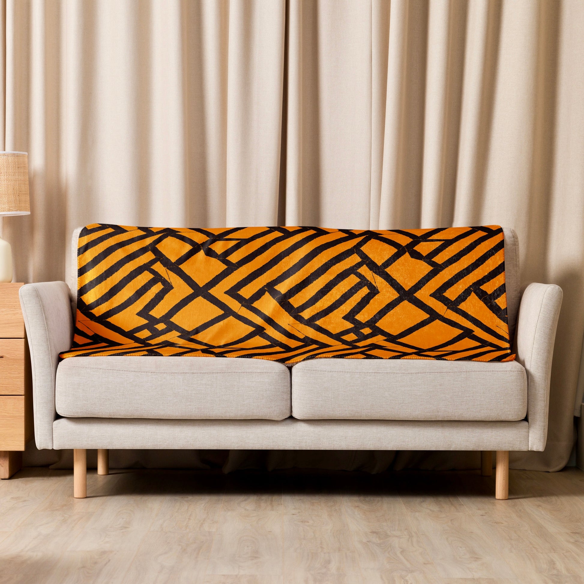 Tintin Studios' orange geometrically patterned Lokoja Sherpa blanket elegantly draped over a cream couch, complementing the modern aesthetic of the living space.