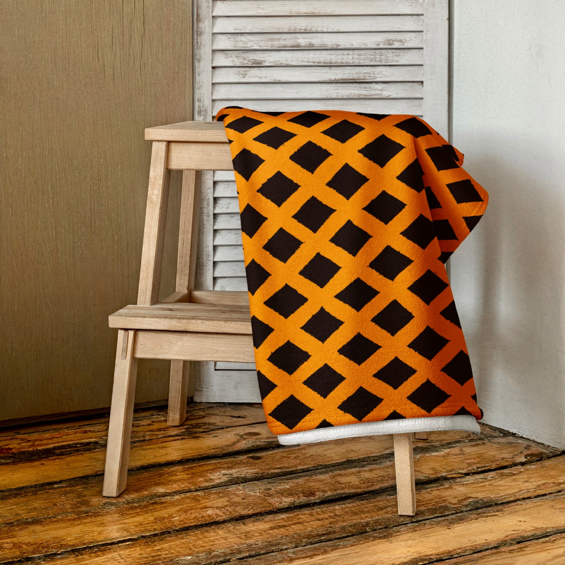 Orange Zaria beach towel from Tintin Studios elegantly folded and draped over a wooden stool, emphasizing its soft texture and tranquil patterns in a vibrant orange hue.