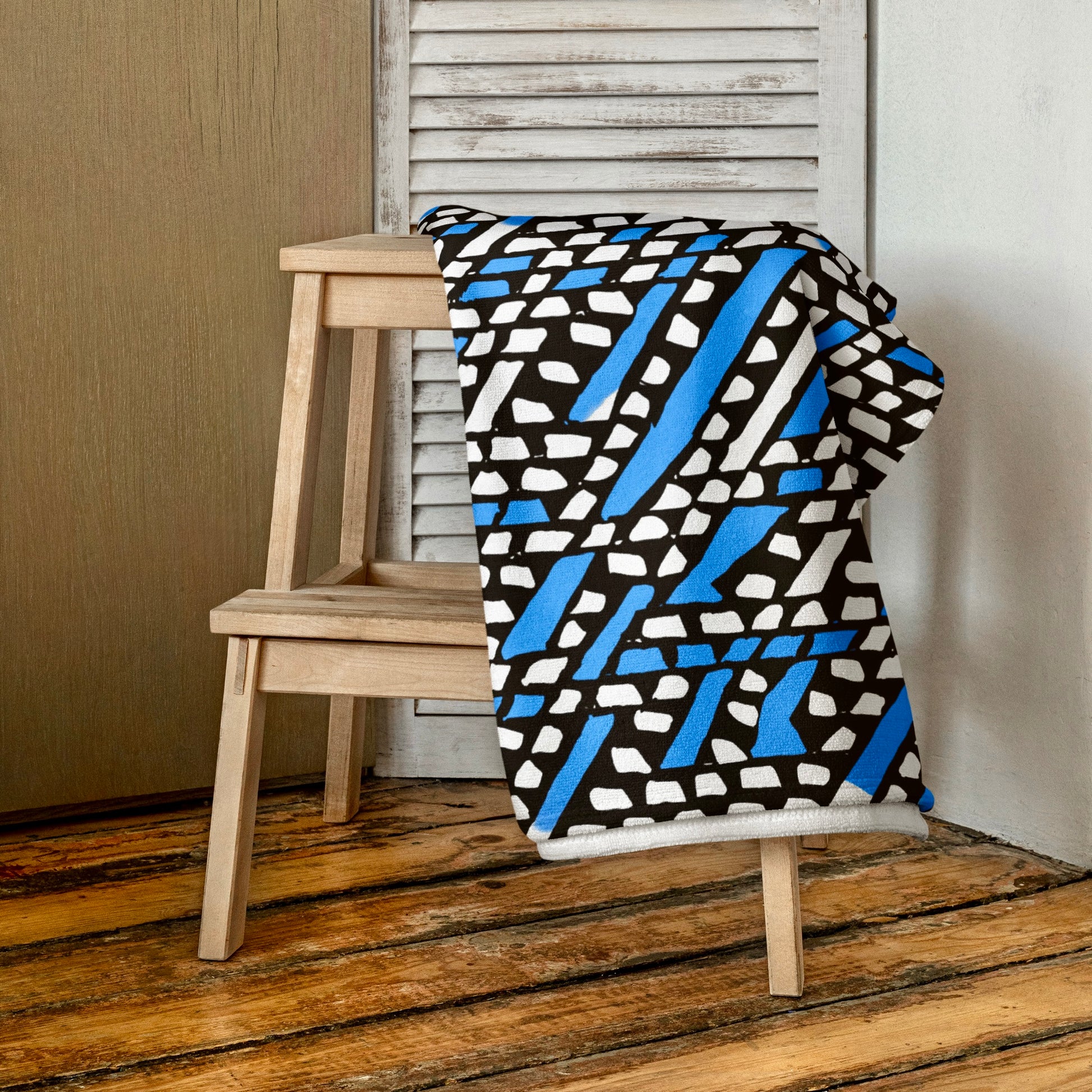 Vibrant blue Ilorin beach towel from Tintin Studios folded on a wooden stool, showcasing its rich patterns and rustic charm.