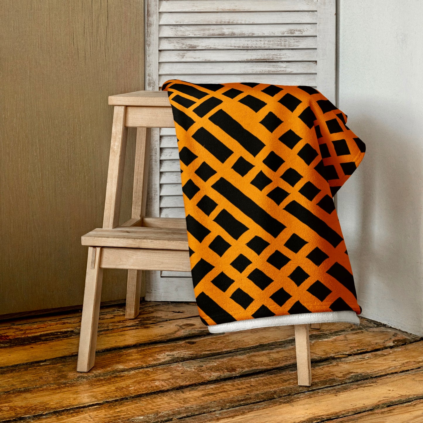 Orange Felele beach towel from Tintin Studios, folded on a wooden stool, accentuating its bold patterns and lively design suitable for a vibrant beach day.