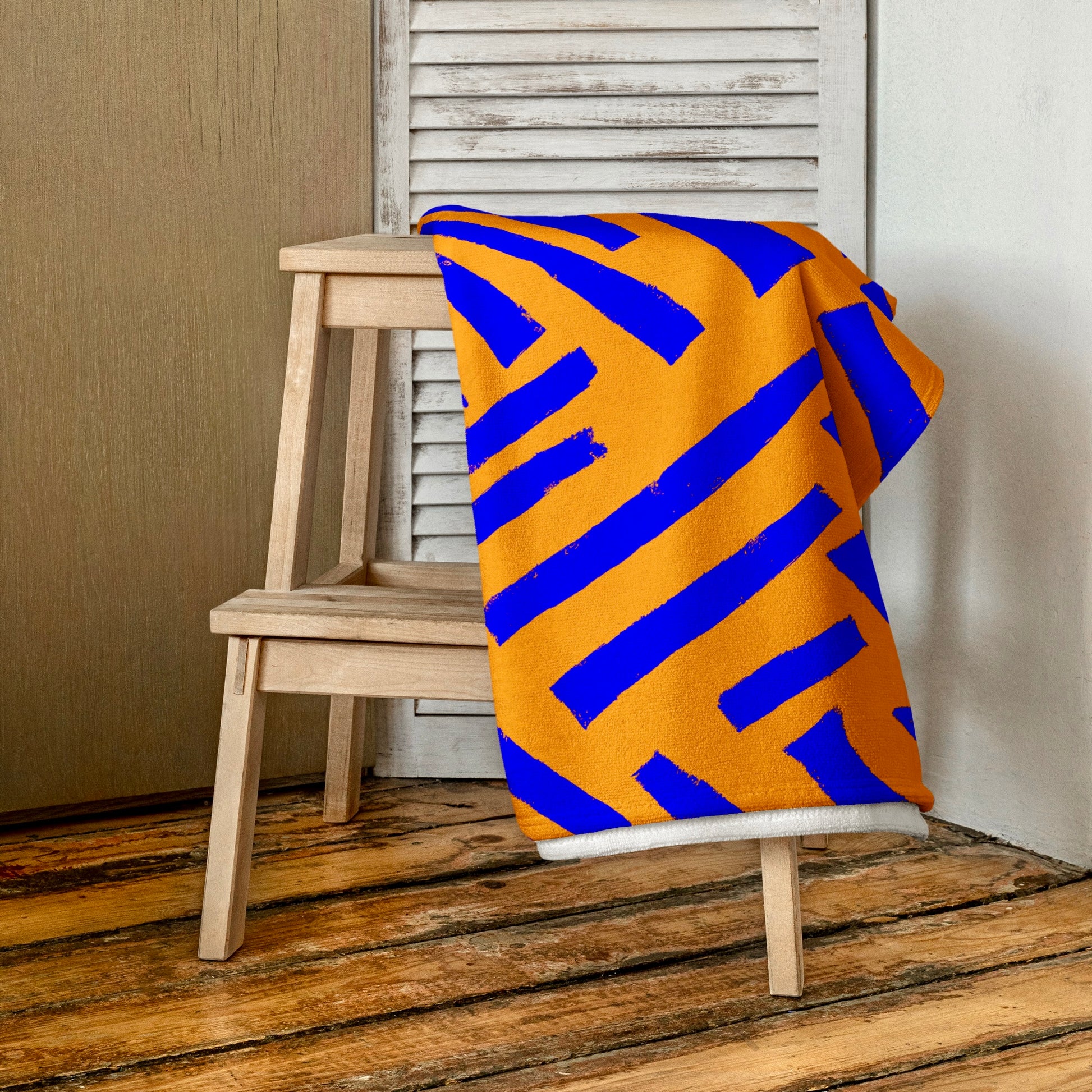 Elegantly folded blue Tutu beach towel from Tintin Studios resting on a wooden stool, revealing the intricate abstract designs that play across its rich blue fabric.