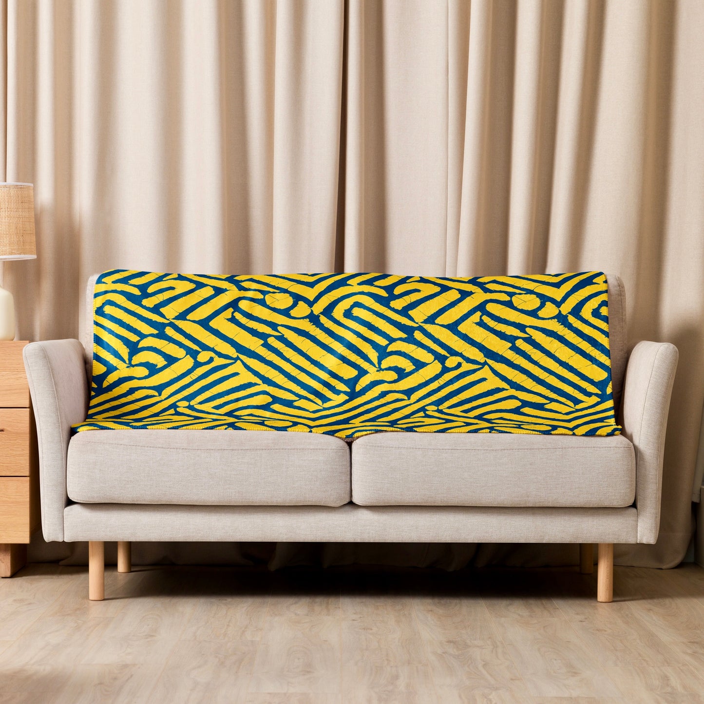 ChiChi Sherpa blanket from Tintin Studios casually draped over a cream couch in a well-lit living room, illustrating the blanket’s vibrant yellow and blue design that perfectly complements modern home décor and offers a cozy, inviting look.