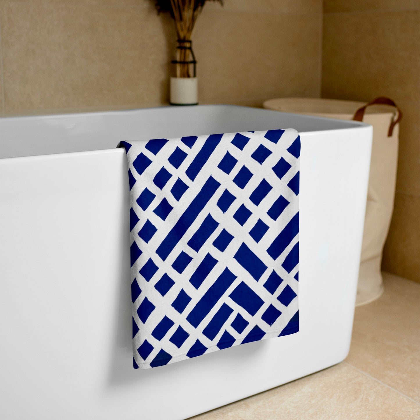 Folded Felele beach towel in blue from Tintin Studios, displayed over a white bathtub, showcasing its unique pattern and vibrant colors ideal for a lively beach day