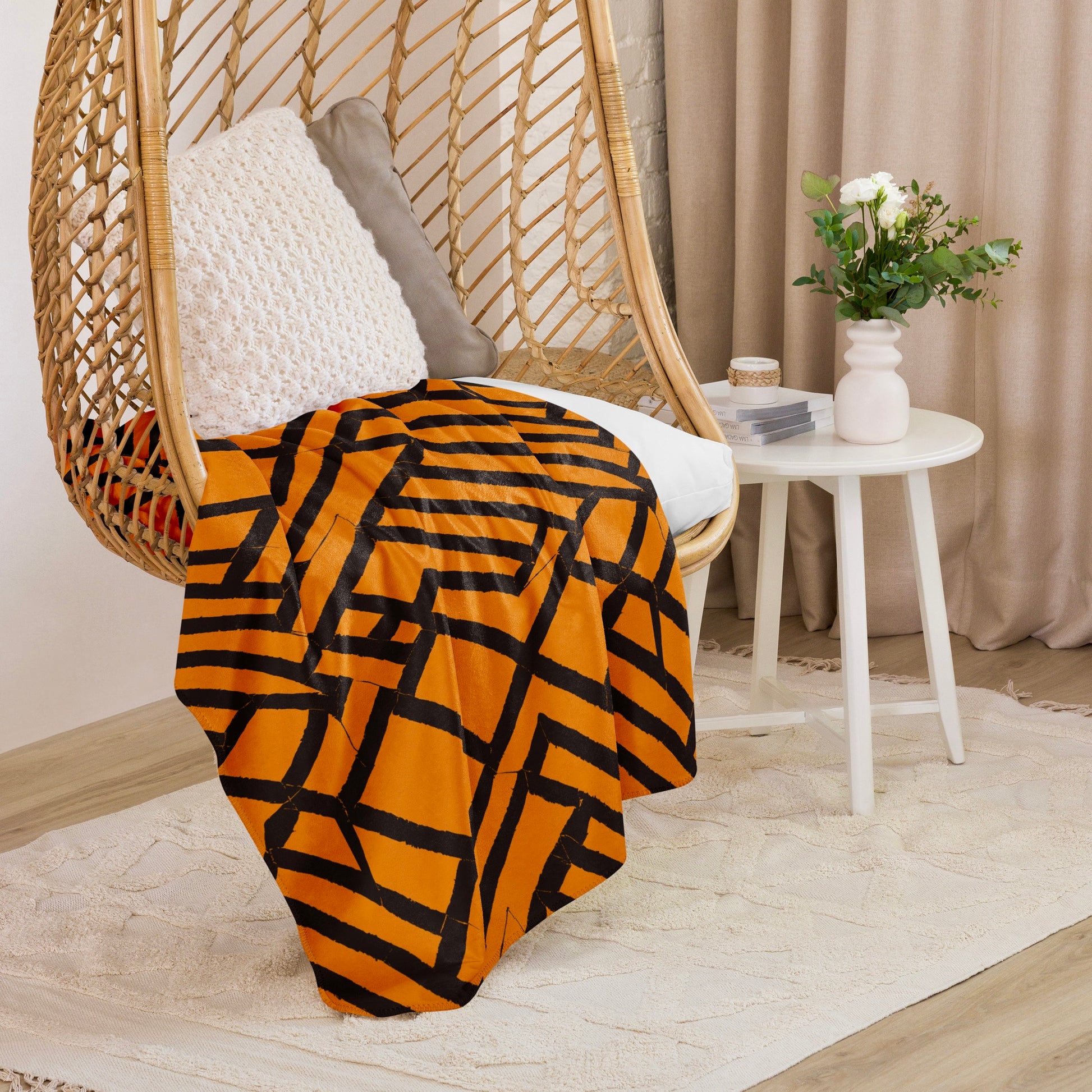 Lokoja Sherpa blanket from Tintin Studios featuring geometric orange and black patterns draped on a wicker chair, enhancing the ambience with its contemporary style and snug feel.