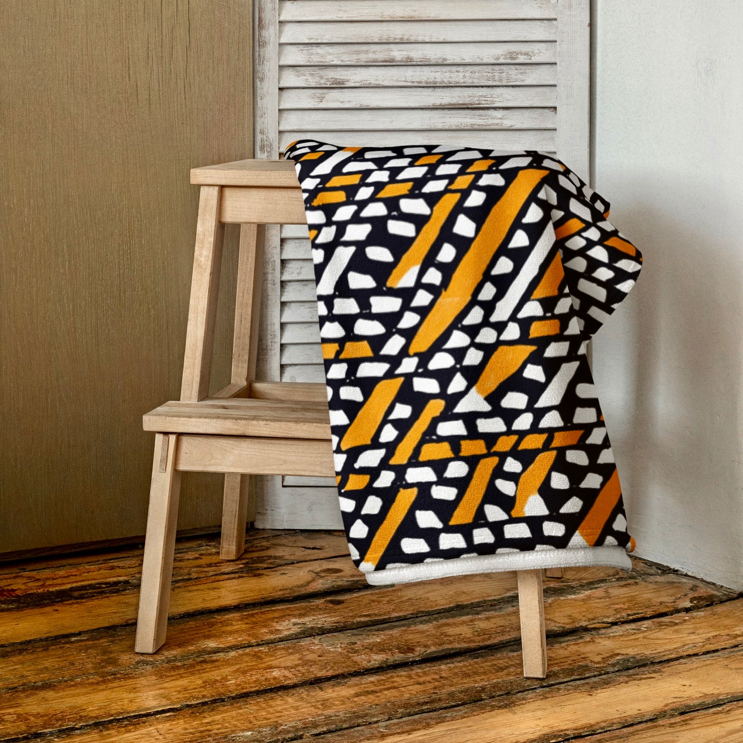 Rustic orange Ilorin beach towel from Tintin Studios, folded atop a wooden stool, accentuating its natural patterns and soft texture.