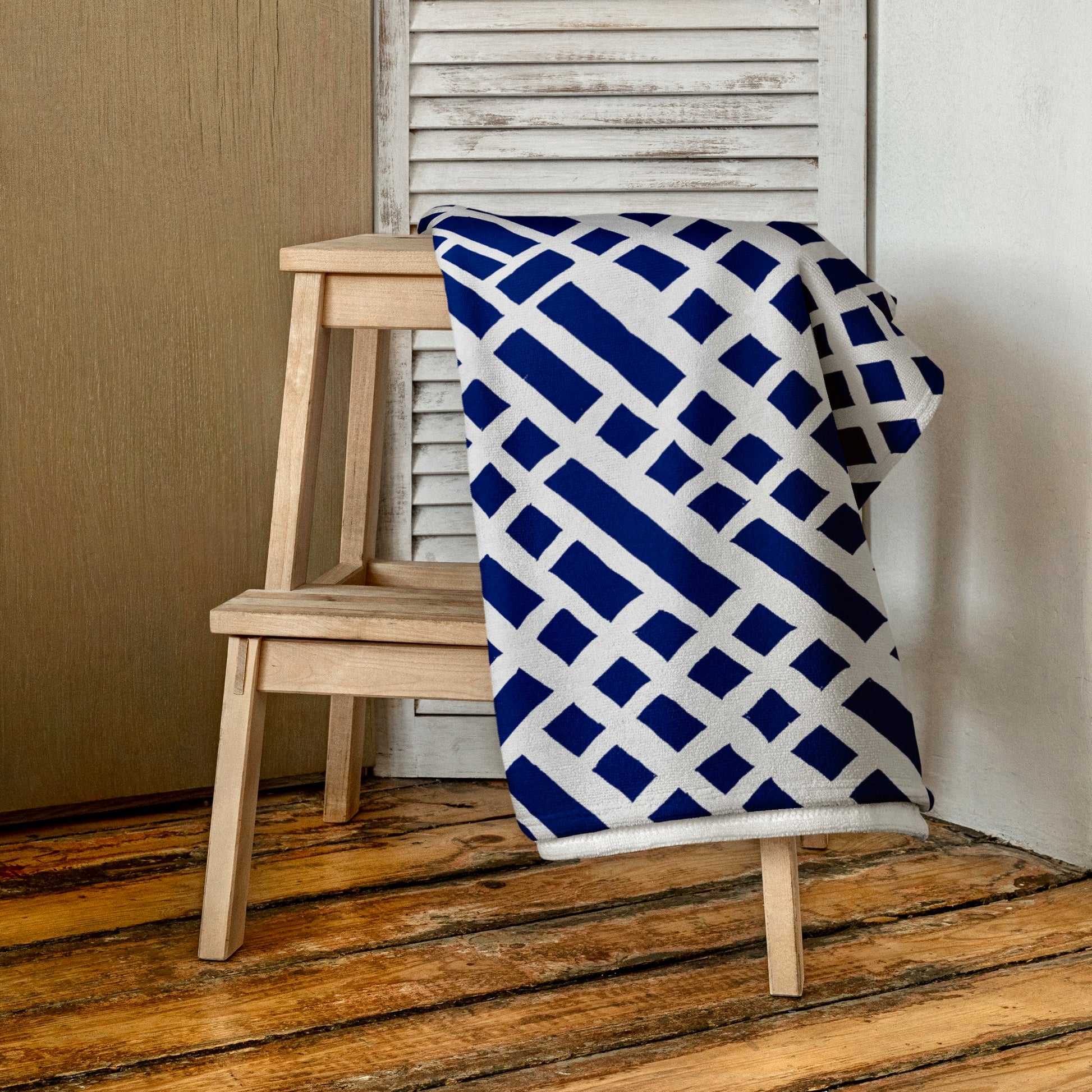 Lush blue Felele beach towel from Tintin Studios, carefully folded on a wooden stool, showcasing its rich, eye-catching patterns.