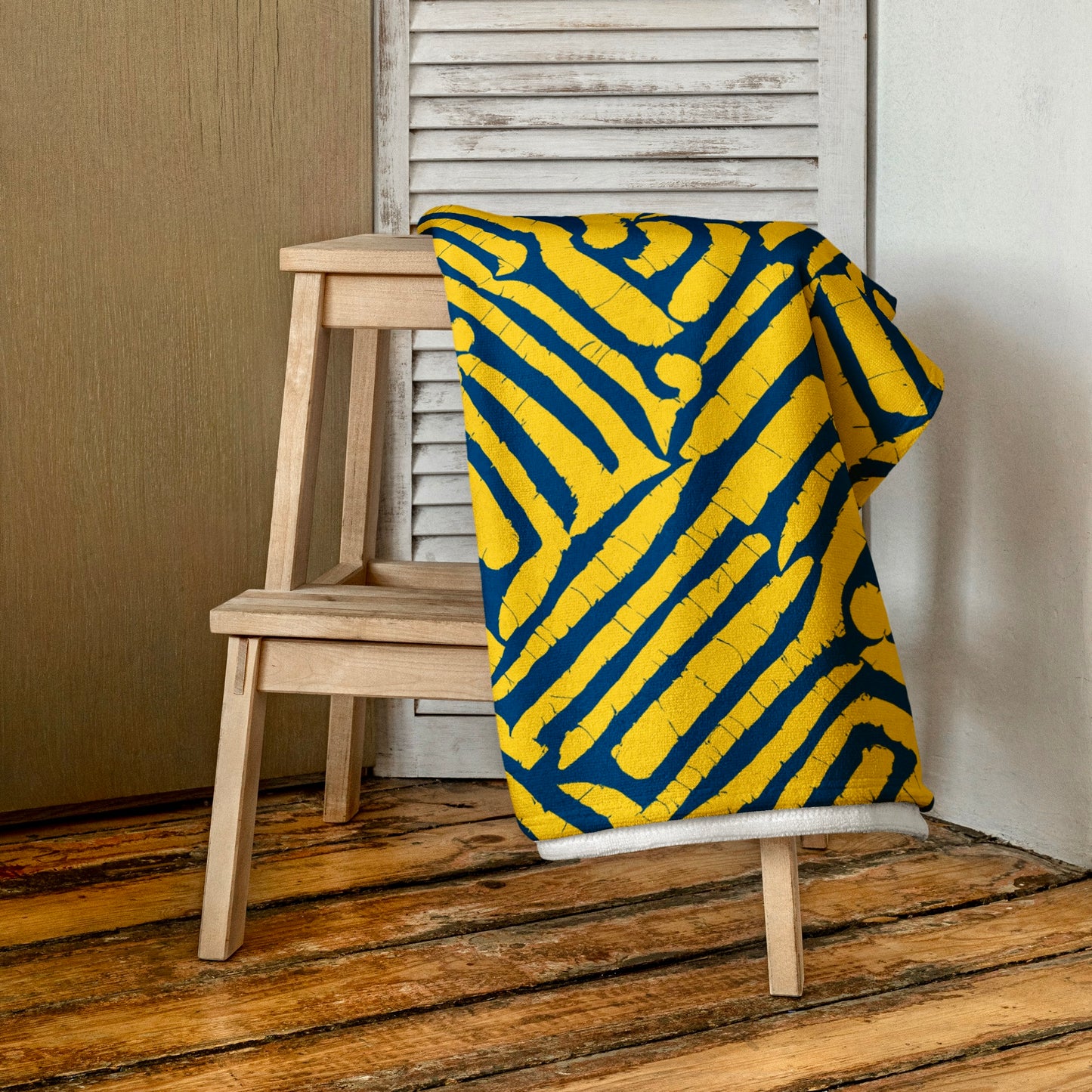 Blue ChiChi beach towel from Tintin Studios folded on a wooden stool, emphasising its lively design and plush texture.