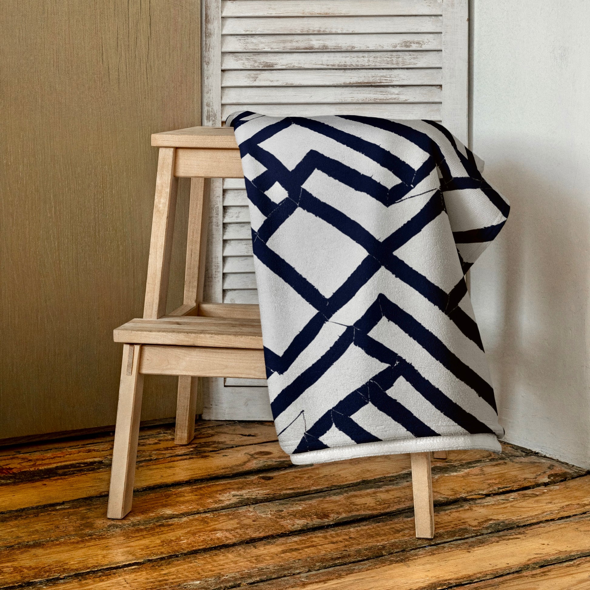 Folded blue Lokoja beach towel from Tintin Studios draped gracefully over a wooden stool, displaying the detailed geometric design and vibrant blue hues that enhance its aesthetic appeal.