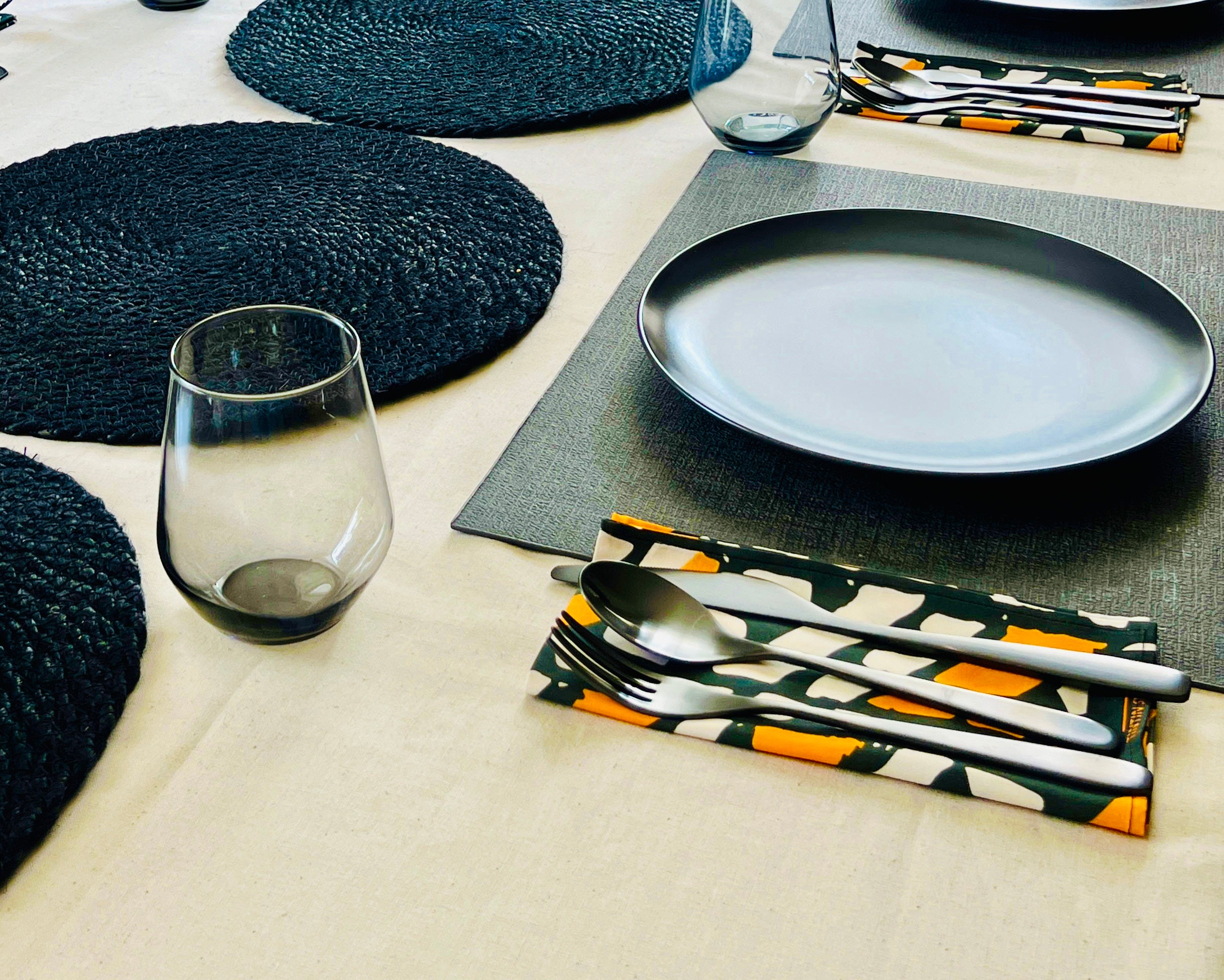 Stylish dining table with Tintin Studios' Ilorin cloth napkins in orange and black, paired with contemporary dinnerware and black woven placemats.